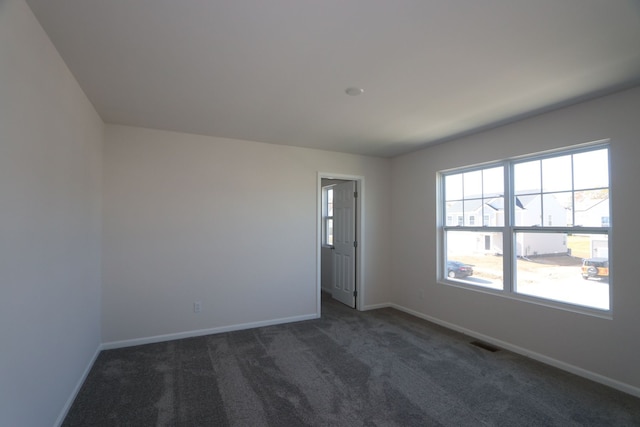 unfurnished room with dark colored carpet, visible vents, and baseboards