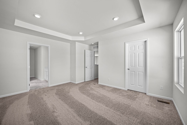 unfurnished bedroom featuring visible vents, baseboards, a tray ceiling, and carpet floors