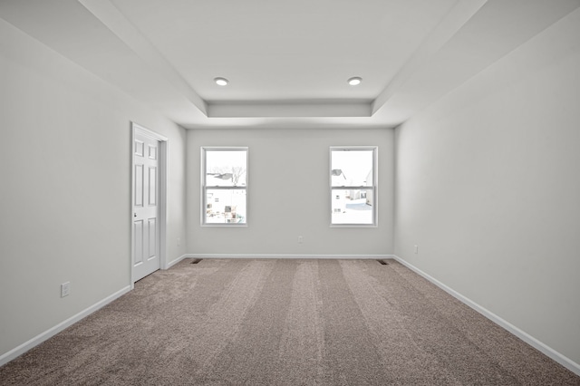 carpeted empty room featuring a raised ceiling and baseboards