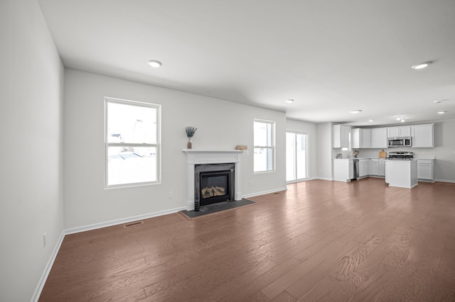 unfurnished living room featuring visible vents, a fireplace with flush hearth, baseboards, and dark wood-style flooring