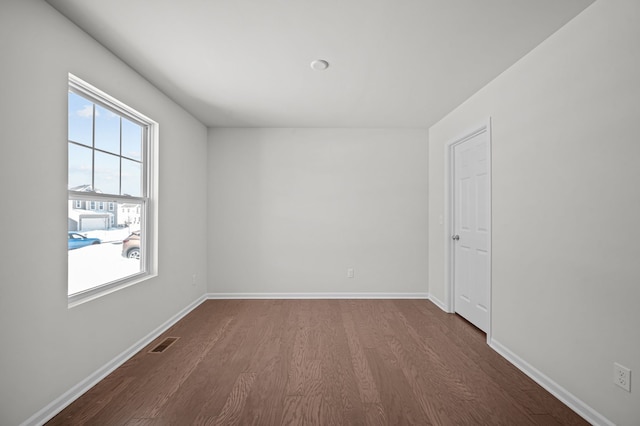 empty room featuring dark wood-style floors, visible vents, and baseboards