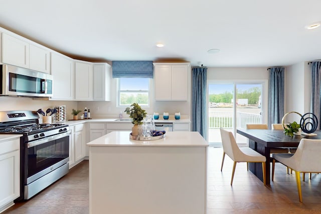 kitchen with light wood finished floors, a sink, stainless steel appliances, light countertops, and a center island