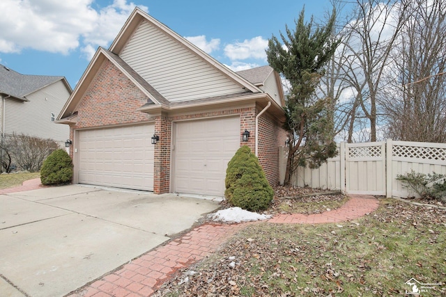 view of side of property featuring driveway, brick siding, an attached garage, and fence