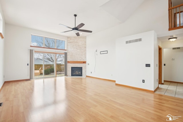 unfurnished living room with light wood-type flooring, visible vents, a stone fireplace, and a towering ceiling