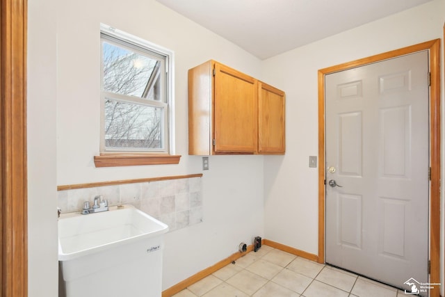 laundry area with light tile patterned floors, a sink, tile walls, baseboards, and cabinet space