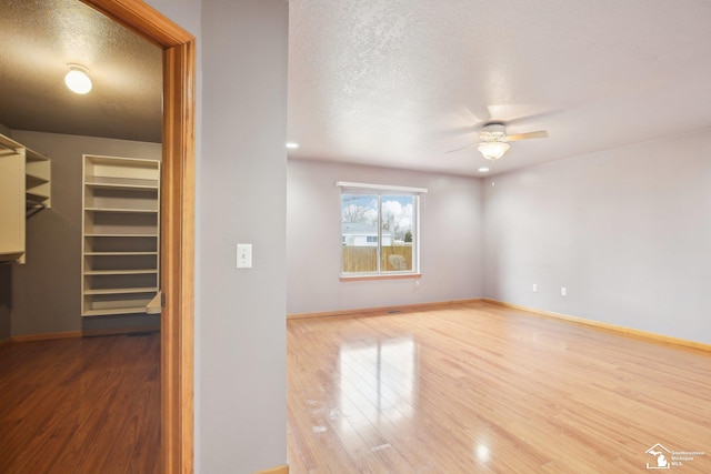 spare room featuring a textured ceiling, wood finished floors, a ceiling fan, and baseboards