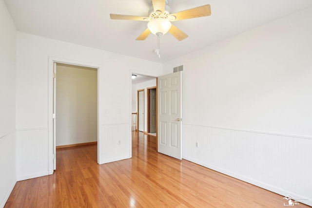 unfurnished bedroom featuring a ceiling fan, wainscoting, visible vents, and light wood-style floors