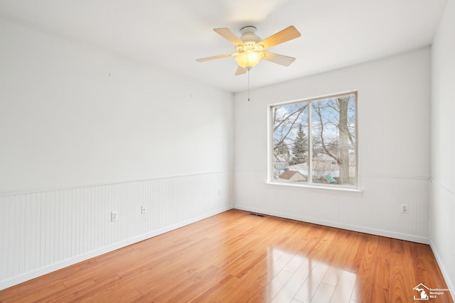 unfurnished room with a wainscoted wall, visible vents, ceiling fan, and wood finished floors