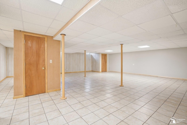 finished basement with light tile patterned floors, a drop ceiling, and baseboards