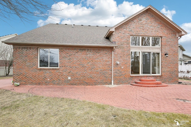 back of property featuring entry steps, a patio, roof with shingles, fence, and brick siding