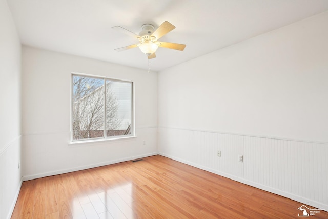 empty room featuring a wainscoted wall, light wood-style flooring, visible vents, and ceiling fan