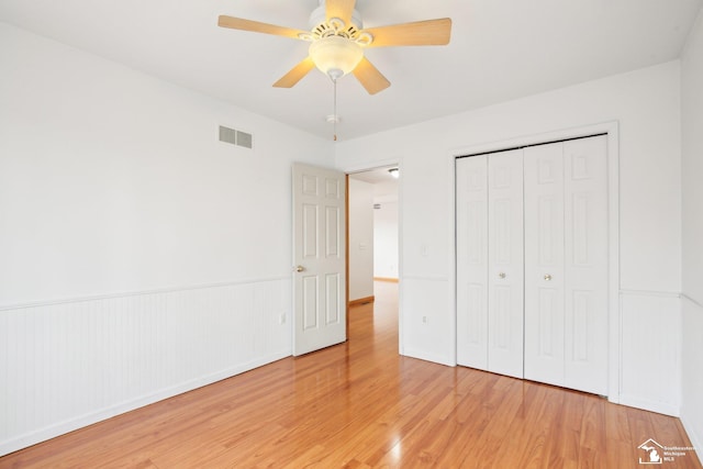 unfurnished bedroom with a wainscoted wall, a closet, visible vents, light wood-style flooring, and a ceiling fan