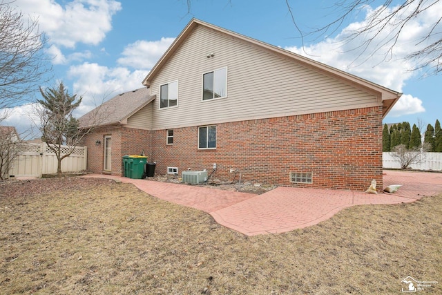 back of property with brick siding, a lawn, central AC, and a patio