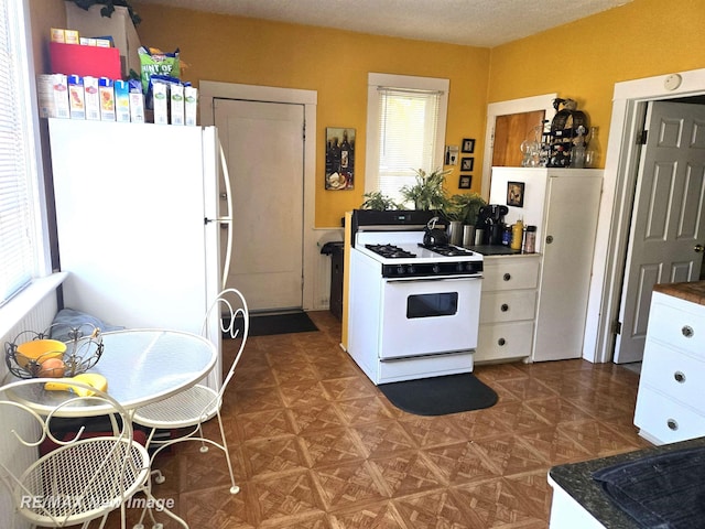 kitchen featuring white appliances, dark floors, white cabinets, and a wealth of natural light