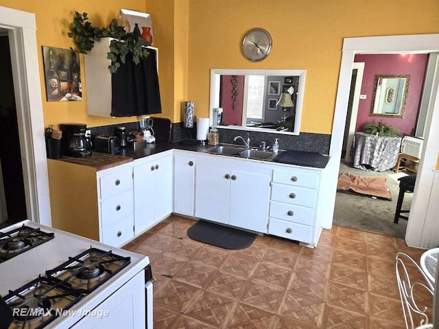 kitchen with white gas stove, dark countertops, a sink, and white cabinets