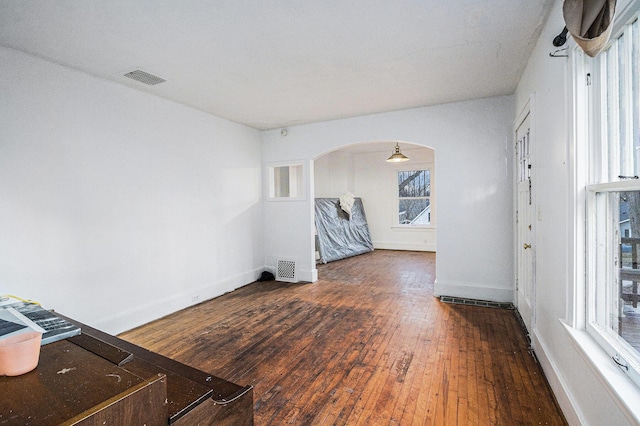 unfurnished living room featuring visible vents, arched walkways, wood-type flooring, and baseboards