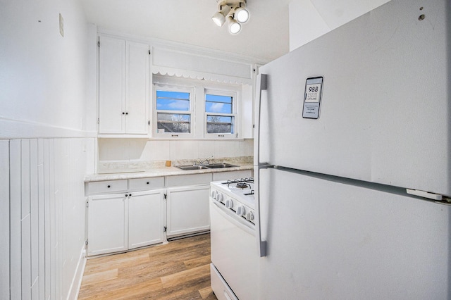 kitchen with white appliances, light wood-type flooring, a sink, and white cabinetry