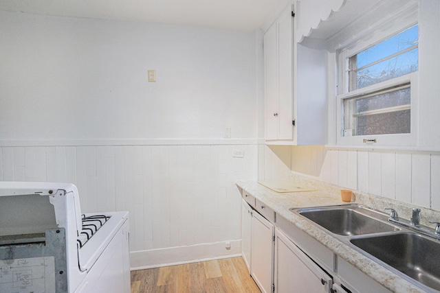 kitchen featuring gas range oven, light wood-style flooring, white cabinets, wainscoting, and a sink