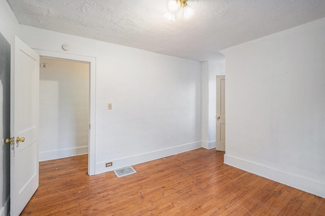 empty room with light wood-type flooring, visible vents, a textured ceiling, and baseboards