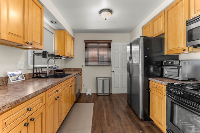 kitchen featuring dark wood-type flooring, a sink, baseboards, appliances with stainless steel finishes, and dark countertops