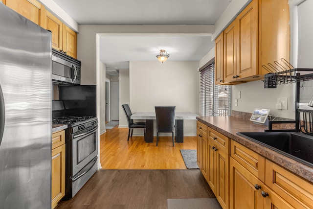 kitchen featuring a sink, baseboards, appliances with stainless steel finishes, dark wood-style floors, and dark countertops