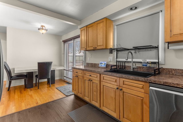 kitchen featuring dark countertops, a sink, wood finished floors, dishwasher, and baseboards