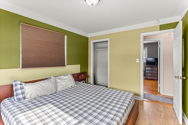 bedroom featuring ornamental molding, a closet, wood finished floors, and baseboards