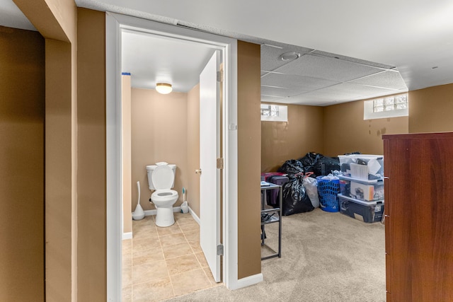 below grade area featuring baseboards, carpet flooring, a paneled ceiling, and tile patterned floors