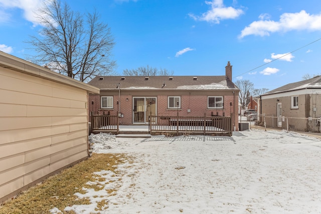 snow covered rear of property featuring a chimney, fence, and brick siding