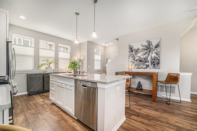 kitchen with dark wood finished floors, appliances with stainless steel finishes, a kitchen island with sink, a sink, and white cabinetry