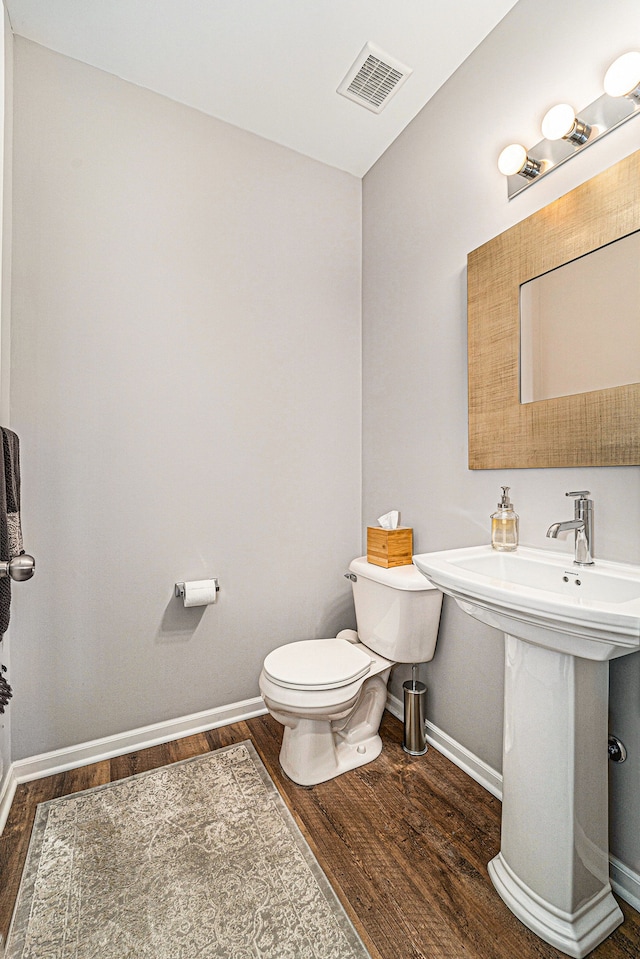 half bath featuring baseboards, visible vents, toilet, and wood finished floors