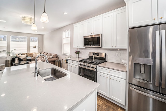 kitchen featuring stainless steel appliances, a sink, open floor plan, hanging light fixtures, and tasteful backsplash