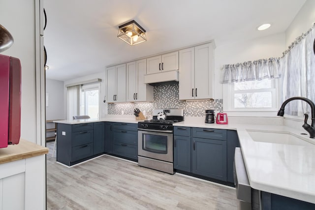 kitchen featuring stainless steel gas range oven, tasteful backsplash, light countertops, under cabinet range hood, and a sink