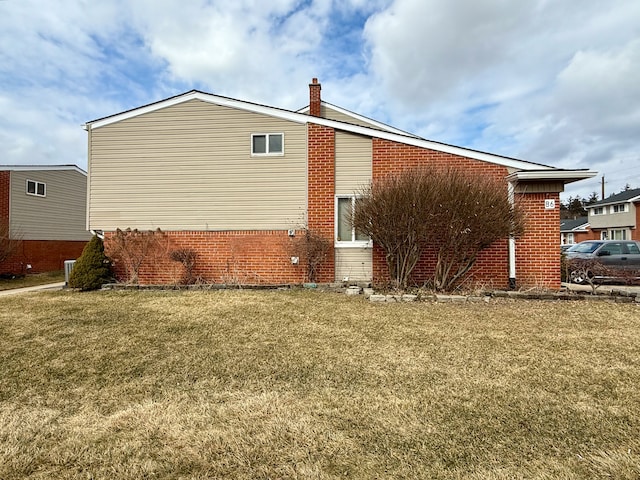 view of side of home with brick siding, a chimney, and a yard