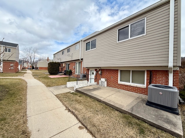 exterior space with central AC, brick siding, a patio, and a lawn