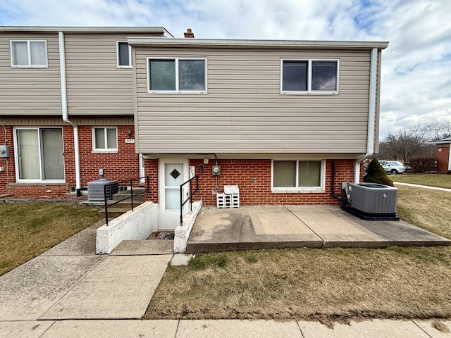 view of front of house featuring a front lawn, cooling unit, and brick siding