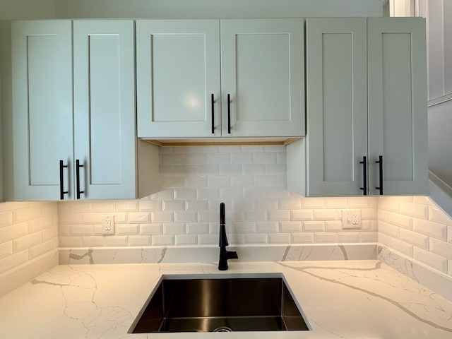 kitchen featuring a sink, backsplash, and light stone countertops