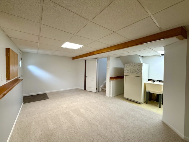 finished below grade area featuring light carpet, baseboards, stairway, freestanding refrigerator, and a paneled ceiling