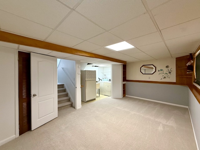 finished basement with a paneled ceiling, light colored carpet, stairway, freestanding refrigerator, and baseboards