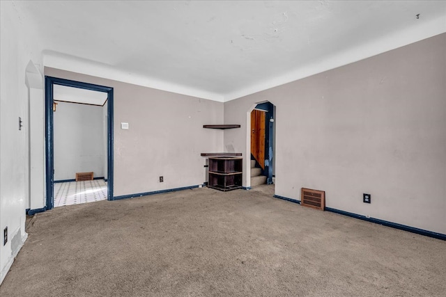 unfurnished living room with carpet floors, arched walkways, visible vents, baseboards, and stairs