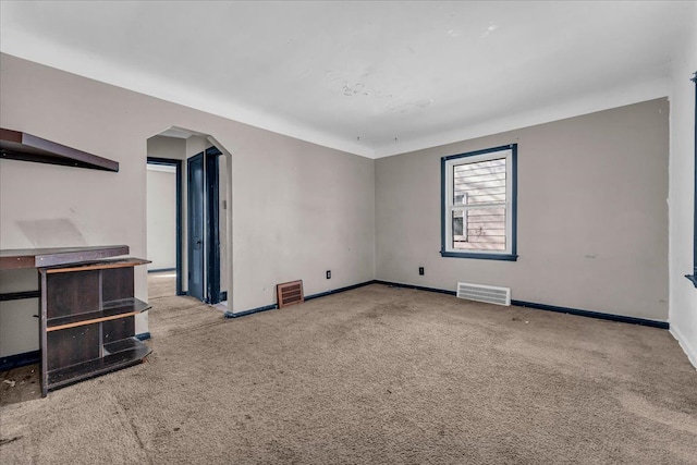 carpeted empty room featuring arched walkways, visible vents, and baseboards