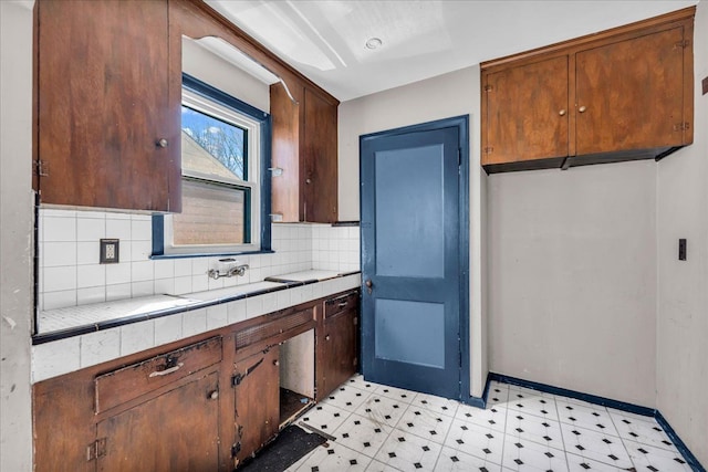 kitchen featuring tile countertops, light floors, tasteful backsplash, a sink, and baseboards