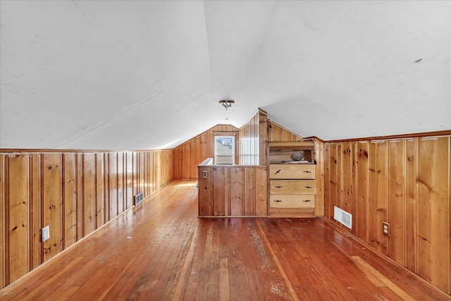 additional living space featuring wood walls, visible vents, vaulted ceiling, and hardwood / wood-style flooring