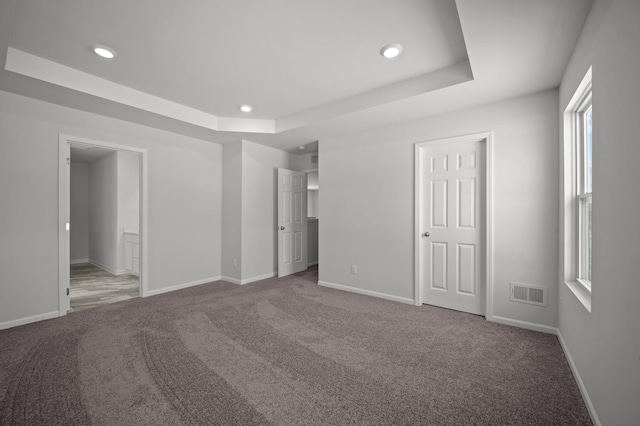 unfurnished bedroom with a raised ceiling, carpet flooring, baseboards, and visible vents