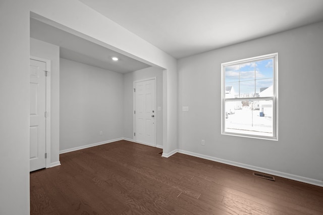 spare room with dark wood finished floors, visible vents, and baseboards