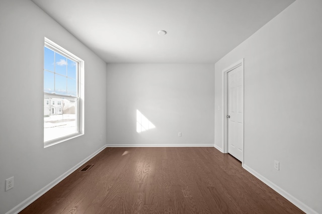 empty room featuring visible vents, baseboards, and dark wood-type flooring