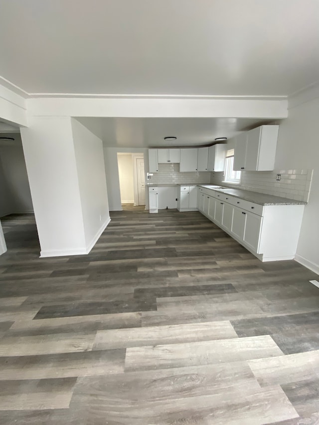 kitchen with dark wood-type flooring, tasteful backsplash, white cabinets, crown molding, and baseboards