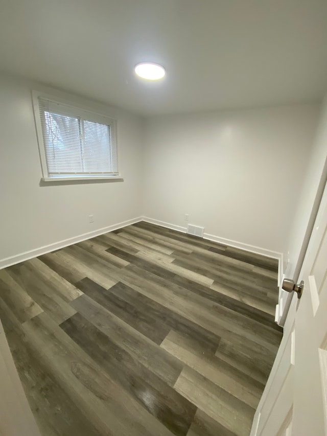 unfurnished room featuring visible vents, dark wood-style floors, and baseboards