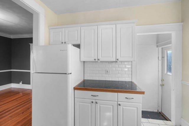 kitchen with dark countertops, decorative backsplash, freestanding refrigerator, wood finished floors, and white cabinetry