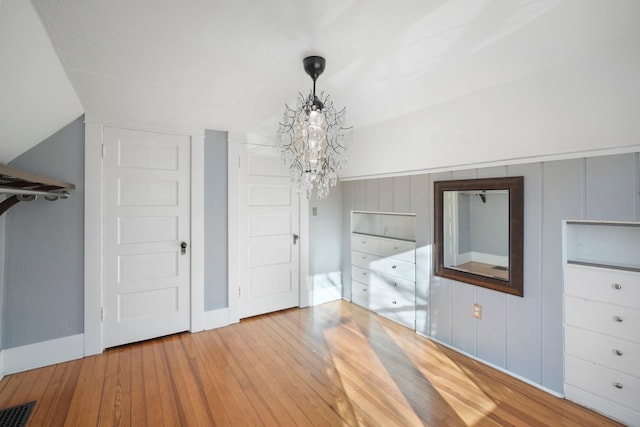 unfurnished bedroom featuring vaulted ceiling, a notable chandelier, visible vents, and wood-type flooring